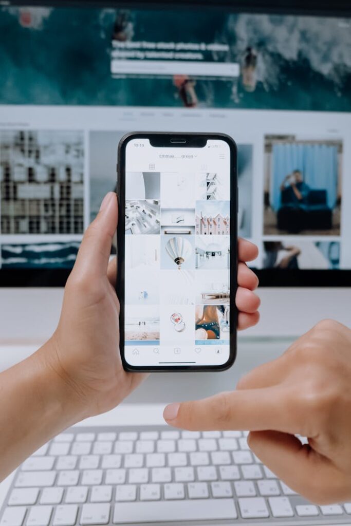 pexels-photo-5082578 Person using smartphone to browse photos, office desktop setup.