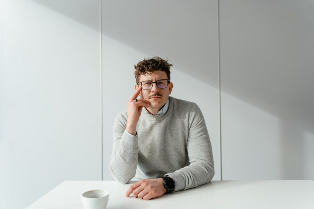 pexels-photo-7255383 Man in glasses sitting at a bright and minimalist office desk, exuding a calm and focused demeanor.